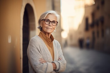 Portrait of smiling senior woman in eyeglasses standing with arms crossed in city