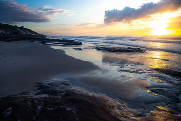 Obraz premium Spectacular orange cloudy sunrise over the pacific ocean at wild ten mile beach. Black rocks campsite, NSW, Australia
