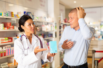 Obraz na płótnie Canvas Woman pharmacist advises man medicine for headache pain. Help in choosing a medicine in a pharmacy