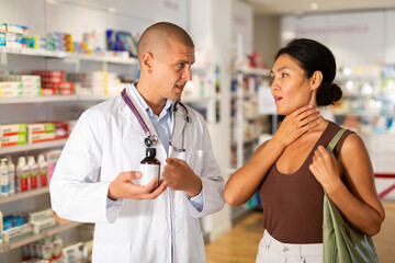 Obraz premium Woman complains to a pharmacist about a sore throat. Help in choosing a medicine in a pharmacy
