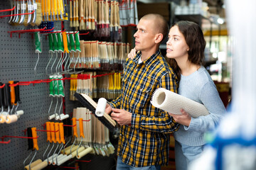 Smiling couple, woman and man, standing with goods in hands in hardware store