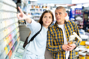 Young cheerful woman and man pointing to shelves at building store