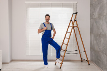 Worker in uniform and stepladder near horizontal window blinds indoors