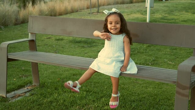 Ni&ntilde;a peque&ntilde;a chiquita bebe hermosa latina sonriente tierna amorosa jugando disfrutando y saludando a la c&aacute;mara sentada en una banca divertida en un hermoso d&iacute;a soleado al atardecer en el parque