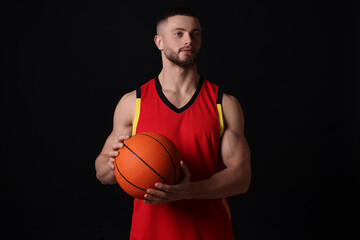 Athletic young man with basketball ball on black background