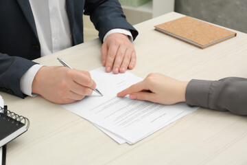 Woman pointing at document and man putting signature at wooden table, closeup