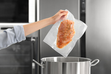 Woman putting vacuum packed meat into pot in kitchen, closeup