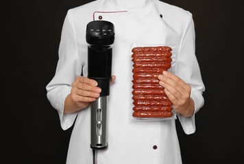 Chef holding sous vide cooker and sausages in vacuum pack on black background, closeup