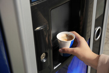 Woman taking paper cup with coffee from vending machine, closeup
