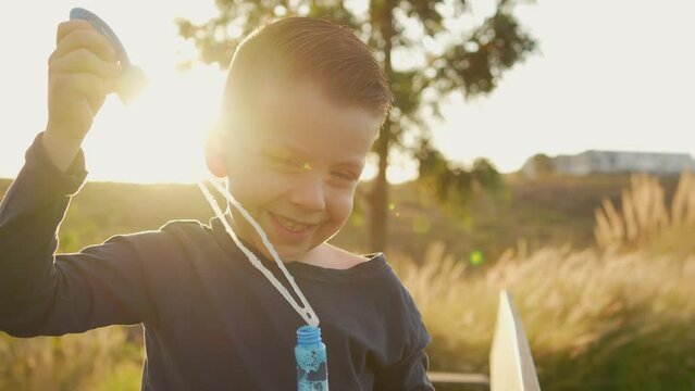 Ni&ntilde;o peque&ntilde;o chico infante latino rubio soplando y haciendo las burbujas jugando y disfrutando de un hermoso d&iacute;a soleado en el atardecer al aire libre en el parque