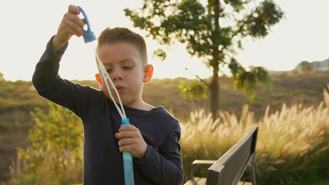 Ni&ntilde;o peque&ntilde;o chico infante latino rubio soplando y haciendo las burbujas jugando y disfrutando de un hermoso d&iacute;a soleado en el atardecer al aire libre en el parque