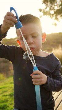 Ni&ntilde;o peque&ntilde;o chico infante latino rubio soplando y haciendo las burbujas jugando y disfrutando de un hermoso d&iacute;a soleado en el atardecer al aire libre en el parque
