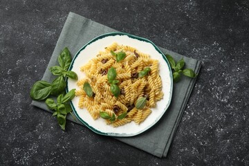 Plate of delicious pasta with anchovies and basil on black textured table, flat lay