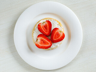 Top view of tasty bruschetta with cream cheese and ripe strawberries on white plate on white background