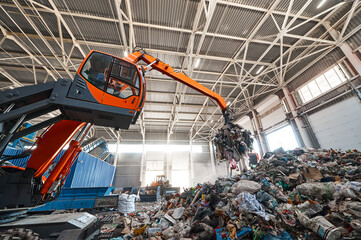 Excavator grabs trash in warehouse of waste processing plant