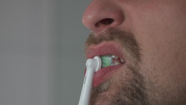 Man brushes his teeth with an electrical tootbrush at morning bathroom before work. Male uses an electric sonic dental cleaning brush. Daily dental hygiene and oral health with eletrical teethbrush. 