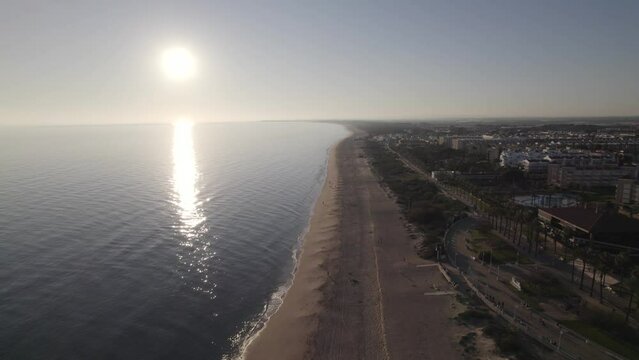 Aerial pullback along Islantilla beach, Sunlight reflection on Atlantic Ocean, Huelva, Andalusia
