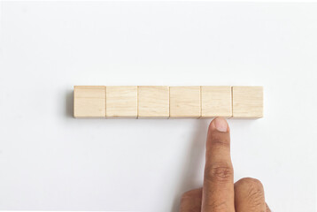 Close-up of a hand pointing with a blank wooden cube on a white background