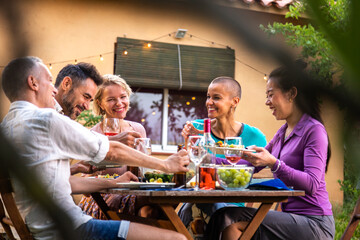 Happy group of friends laughing and eating during garden dinner party.