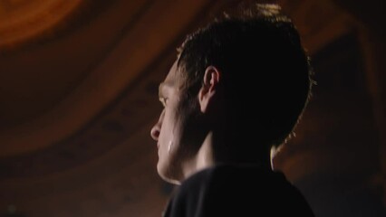 Close up shot of tired ballet male dancer standing on theater stage and training before performance. Sweat flows down his face. Choreography rehearsal. Illuminated theatrical hall. Classical ballet.