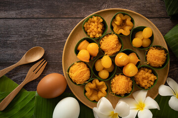 a variety of elegantly beautiful Thai Desserts (Khanom Wan Thai) serving in a wooden plate on a dark wooden table. The bites in gold color and different flower shapes.Thai dessert, Auspicious dessert