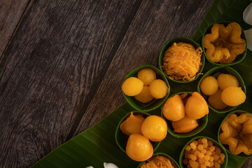 a variety of elegantly beautiful Thai Desserts (Khanom Wan Thai) serving in a wooden plate on a dark wooden table. The bites in gold color and different flower shapes.Thai dessert, Auspicious dessert