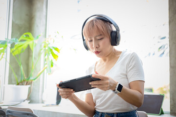 Asian woman wearing headset and playing videogame on a portable gaming console at cafe.