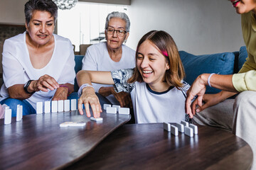 latin family playing domino game with grandmother and daughter at home, three generations of women...
