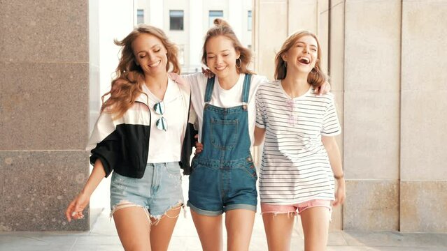 Three young female hipster friends.  girls dressed in summer jeans shorts. Women smiling. Having fun and going crazy. Models posing in the street at sunset.