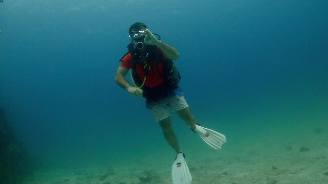 Under Water Film Sail rock in Thailand April 2023 -single newcomer scuba diver gives the ok sign towards the camera - hovering just about the ocean floor