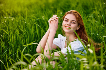 adorable, smiling woman sitting in nature relaxing in tall grass looking at camera