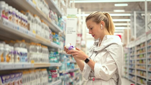 40s woman check yogurt expire date. Person choose better fresh drinks. Girl read bottle label. Buyer look food shelf life. Lady pick up buy diet beverage. Health care store. Client count meal calorie.