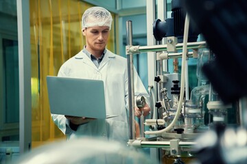 Apothecary scientist working with laptop near CBD oil extractor and a scientific machine used to...