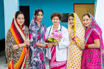 Fototapeta na wymiar Group of traditional Indian women wearing sari thanking and greeting doctor by giving bouquet of flower,Concept of woman empowerment
