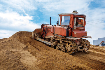 An old orange bulldozer performs work to level the sandy soil