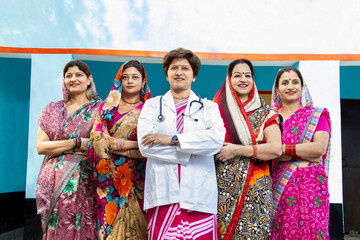Confident Lady doctor standing with group of traditional rural indian women wearing sri with their arms cross. Concept of woman empowerment. Low angle shot.
