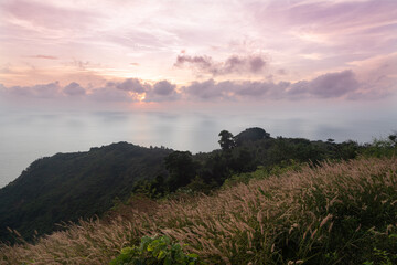 Obraz premium Panoramic view from Promthep Cape sunset viewpoint in Phuket island in Thailand. Purple skies above endless foggy abyss. Tropical hills covered with yellow tall grass look like wheat in the foreground