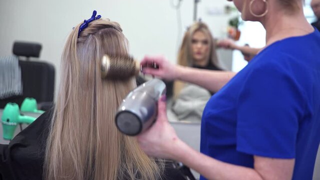 Hairdresser wearing blue uniform dries client's long hair