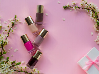 Set of cosmetic nail polishes on pink background with cherry flowers, gift box and copy space....