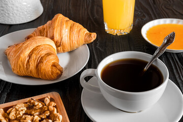 Coffee cup with croissant on a rustic dark wooden table. Food series. Two tasty fresh croissants, jam, orange juice. Continental breakfast served with freshly baked pastry. Close up view, Good morning