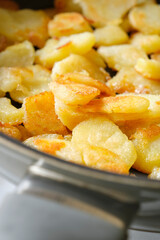 Closeup of yellow fried or baked potatoes with a crispy brown crust in a frying pan. Vertical image with selective focus.