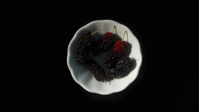 I quickly spread the mulberry berries on a white plate. Rotating top view. Isolated