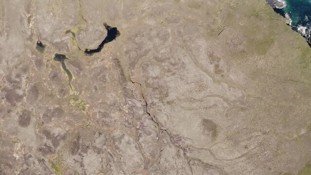 Drone shot of a moorland featuring various small lochs and peat bogs. The shot moves over some rocky cliffs. Seabirds are visible. Filmed in Ness on the Isle of Lewis, part of the Hebrides, Scotland.