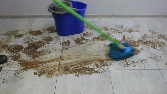 A male cleaner washes the ceramic floor in the hallway with a mop from dirty footprints. Wet cleaning of the room.