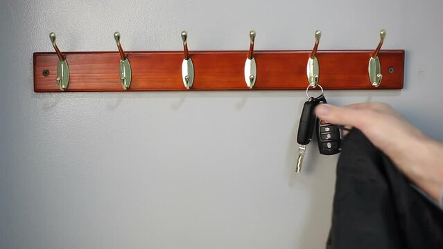 A man takes a jacket and car keys from a hanger. The man leaves the house.