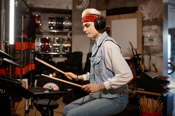 Hipster woman musician wearing headphones playing drum set at music shop