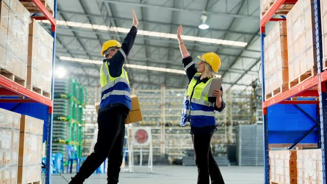 Retail Storehouse full of shelves with goods in cardboard boxes, Young man and woman warehouse worker wearing vest and helmet safety hand touching hi five for success