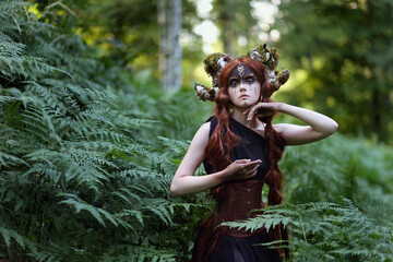 Naklejka premium Beautiful red haired girl with braided hair and dark faceart with mossy horns among fern. Faitytale portrait of faun in dark forest