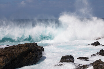 A wave breaks hard on the reef's coastline on a sunny day