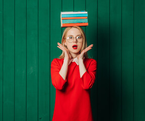 Stylish blond hair woman in red dress with book on head on green wooden background